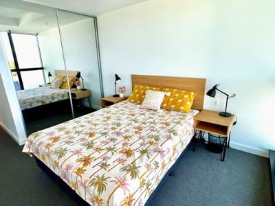 Modern bedroom with tropical bedspread, nightstands, and mirror at UniLodge Zamia Apartments.