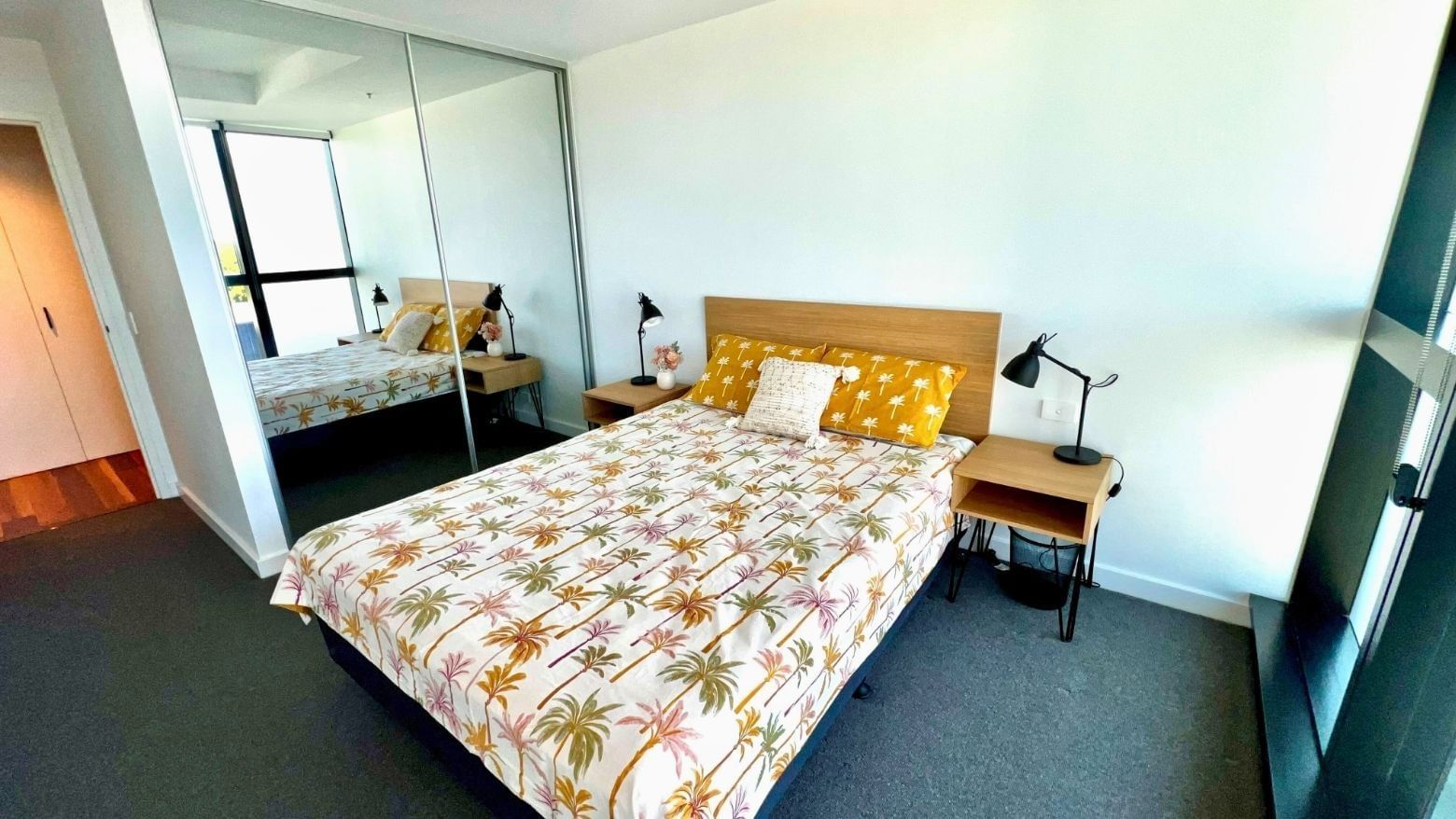 Modern bedroom with tropical bedspread, nightstands, and mirror at UniLodge Zamia Apartments.