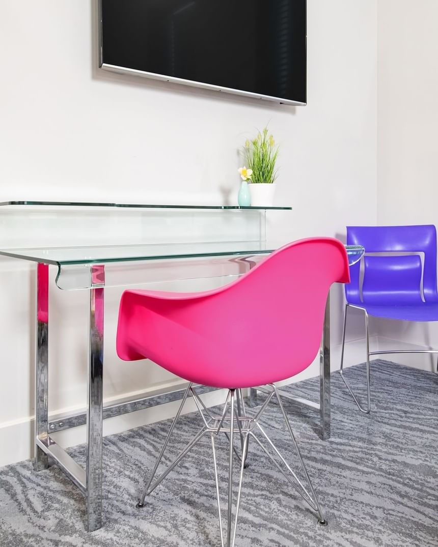 pink chair sitting at glass desk with a purple chair in corner a