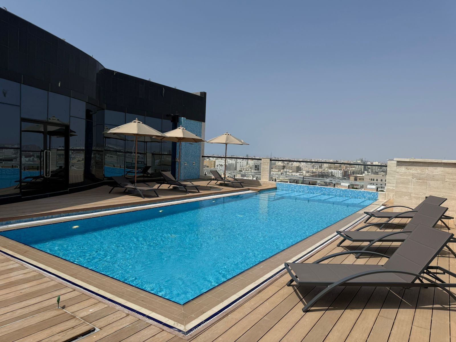 Sun loungers by a rooftop pool under beige umbrellas surrounding the deck area at Warwick Jeddah Hotel & Spa