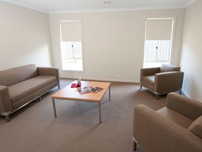 Living room with couch, coffee table, and chairs at La Trobe University Regional Housing – Shepparton.