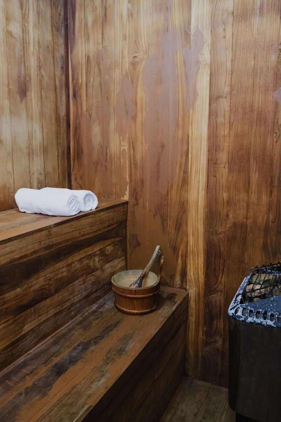 Interior of a wooden sauna with a rolled towel, bucket, ladle, and heater in Hotel Las Olas