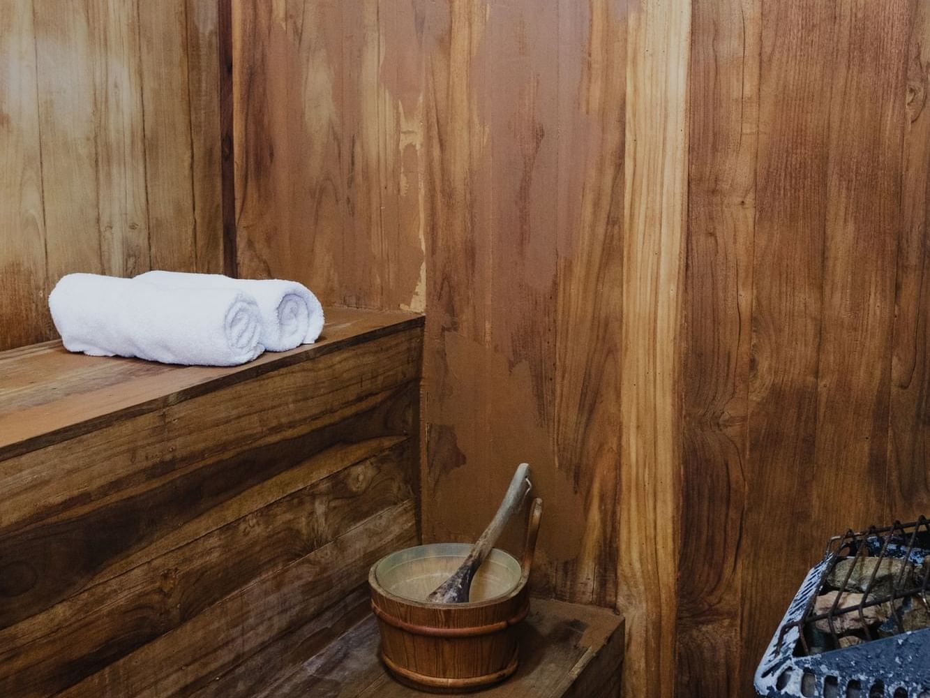 Wooden sauna with a rolled towel, bucket, ladle, and stone heater at Las Olas Beach Resort