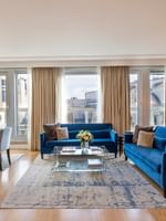 Blue sofas surrounding a glass coffee table by a dining set in The Champs-Élysées Suite at Warwick Paris Champs Elysées