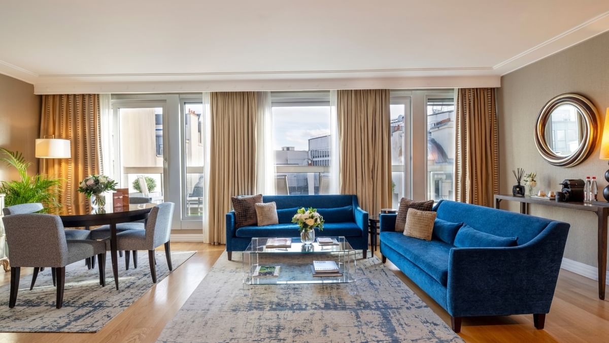 Blue sofas surrounding a glass coffee table by a dining set in The Champs-Élysées Suite at Warwick Paris Champs Elysées