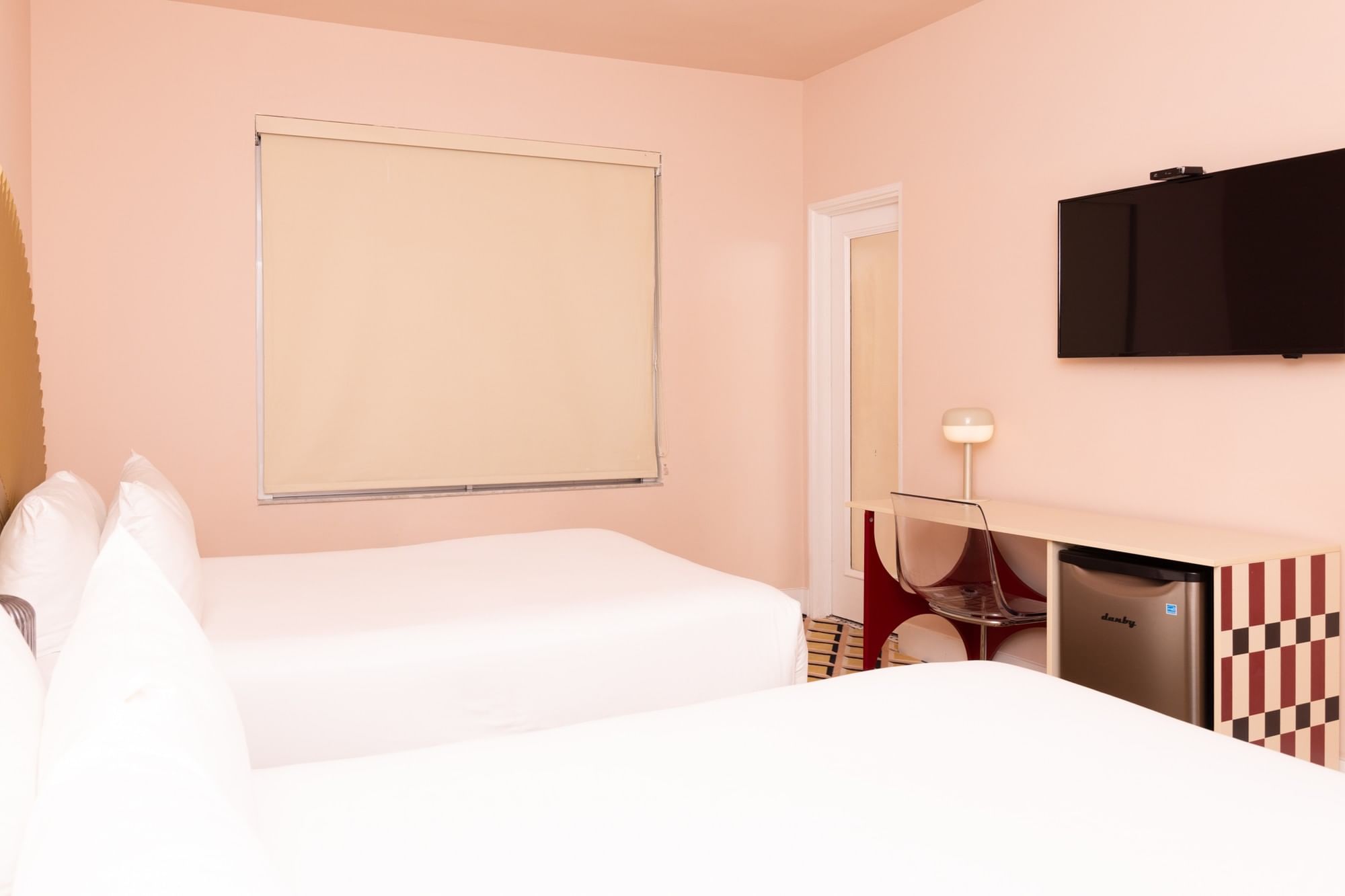 A wide view of a hotel room with two beds, a TV, and a mini-fridge.