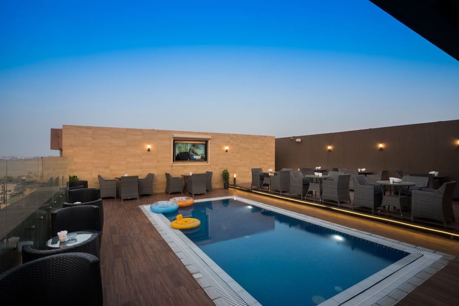Woven chairs by small tables surrounding a rectangular pool in Sky View Café at Naviti By Warwick Dammam 
