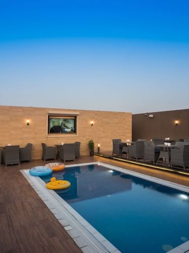 Woven chairs by small tables surrounding a rectangular pool in Sky View Café at Naviti By Warwick Dammam