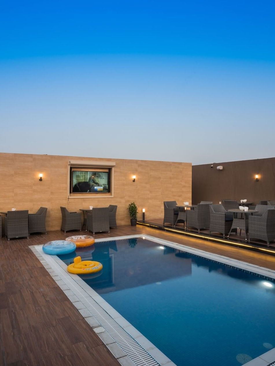 Woven chairs by small tables surrounding a rectangular pool in Sky View Café at Naviti By Warwick Dammam