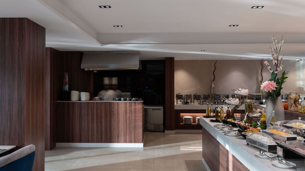 Chefs at a cooking station by a salad buffet under recessed ceiling lights in Rosa Restaurant at Warwick Al Taif Hotel