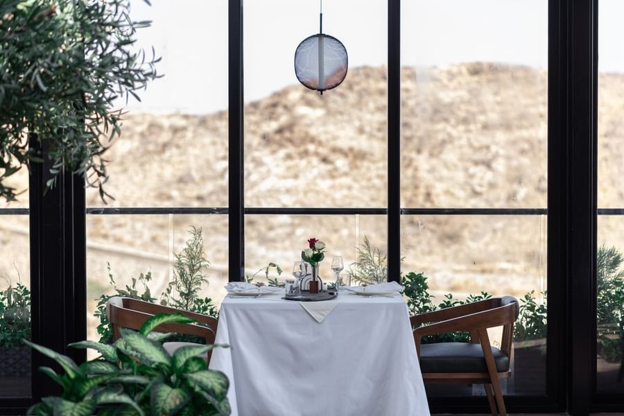 Set table with roses by a large window overlooking a rocky hill in Karkan Restaurant at Warwick Al Taif Hotel