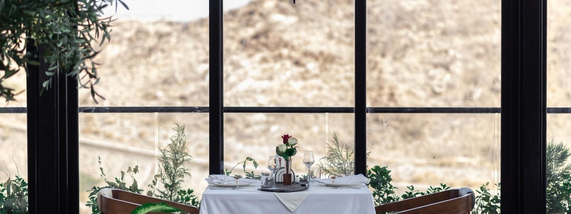 Set table with roses by a large window overlooking a rocky hill in Karkan Restaurant at Warwick Al Taif Hotel