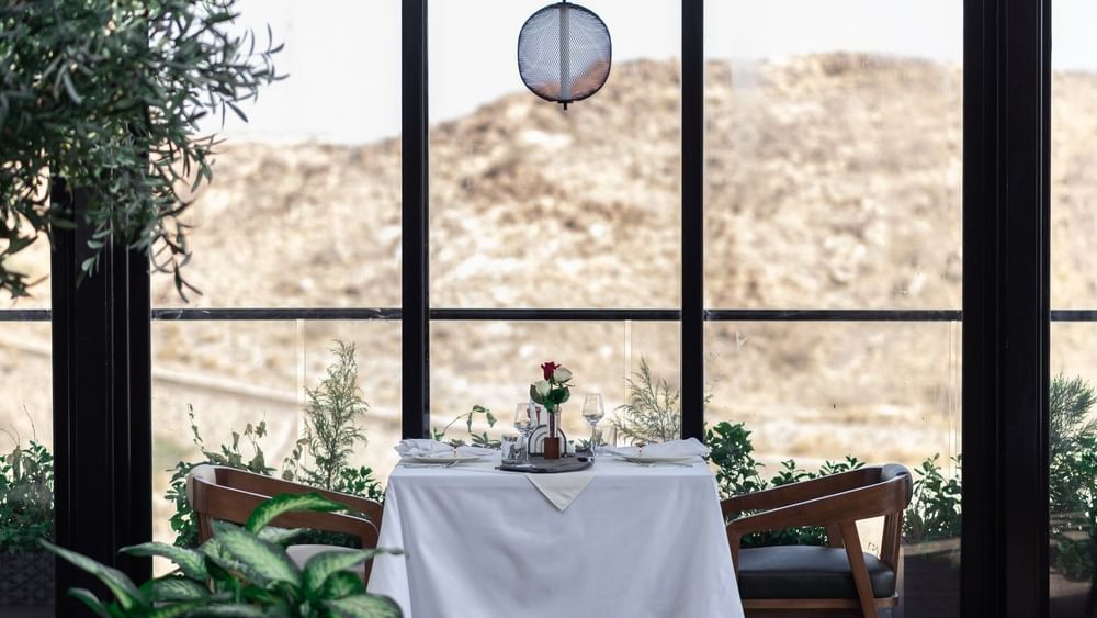 Set table with roses by a large window overlooking a rocky hill in Karkan Restaurant at Warwick Al Taif Hotel