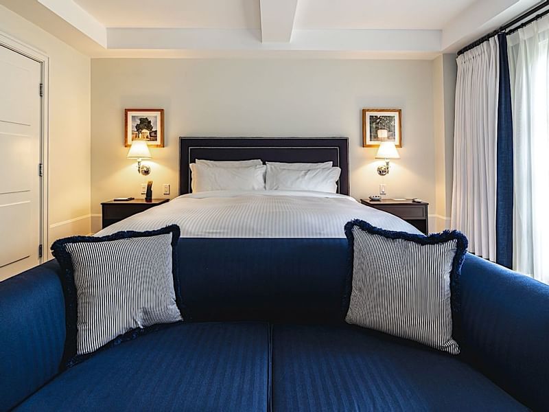 Cozy king bed and blue sofa with striped pillows at El Prado Hotel, creating a relaxing ambiance