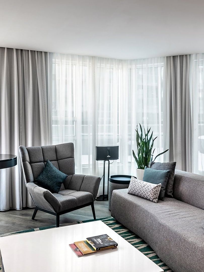 Living area with a grey sofa, armchair, and table set against floor-to-ceiling windows at Warwick Le Crystal Montreal 