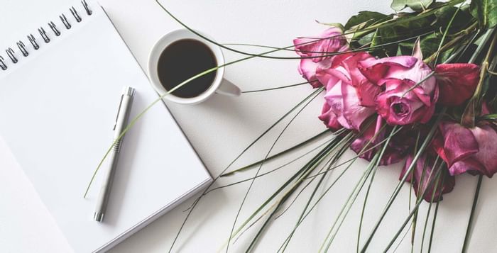 A notepad, pen, coffee cup and pink roses on a white surface at Sunway Hotel Georgetown