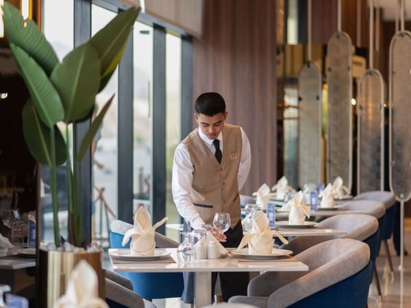 Waiter serving glass on a dining table in Rosa Restaurant at Warwick Hotel Al Taif