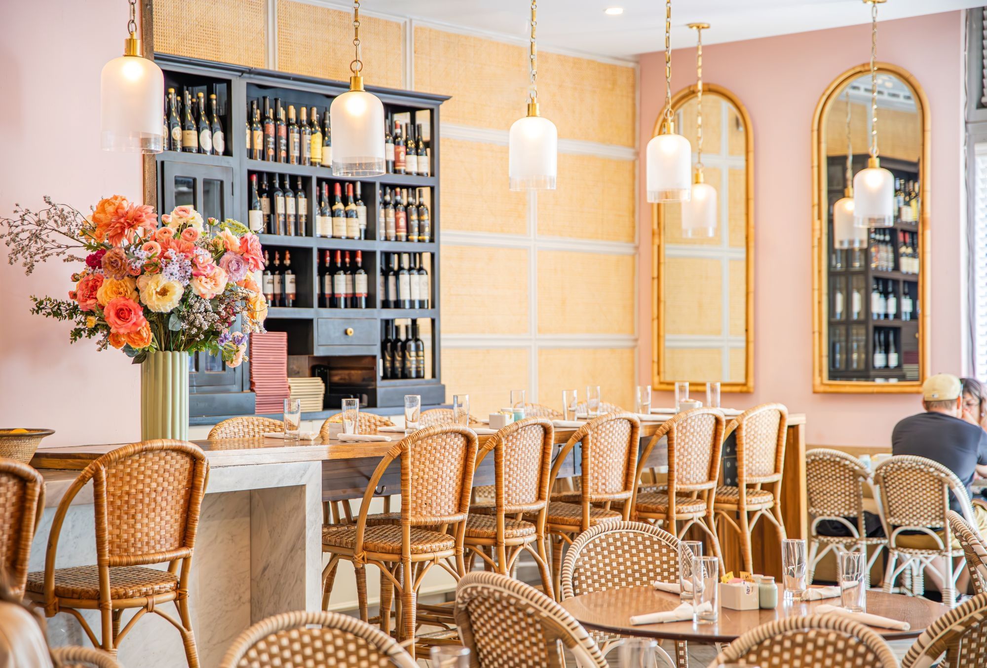 a dining area with wicker chairs, wine glasses, and flowers on the table