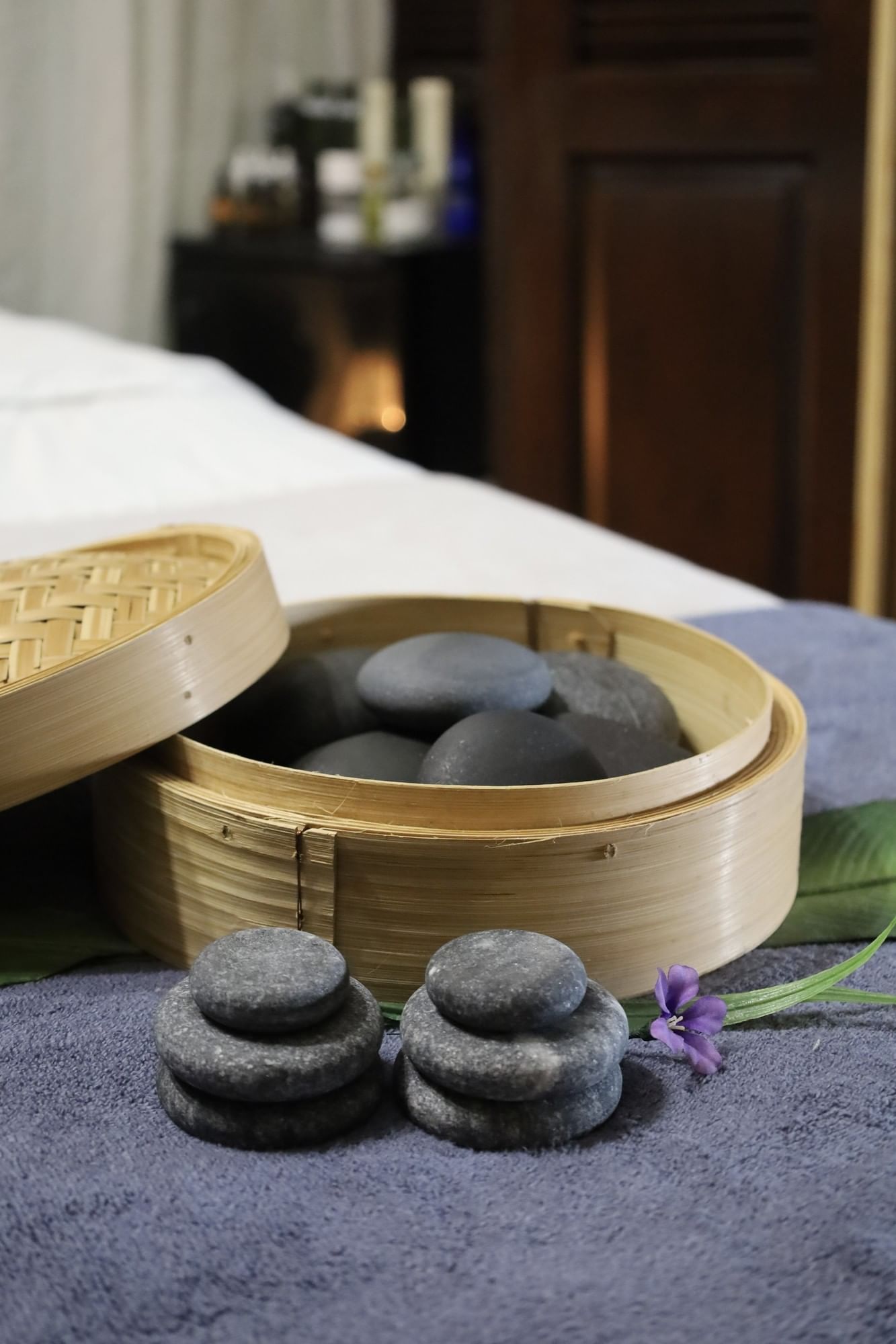 Smooth black stones in a bamboo steamer by a purple flower under soft light at Arlington Resort Hotel & Spa
