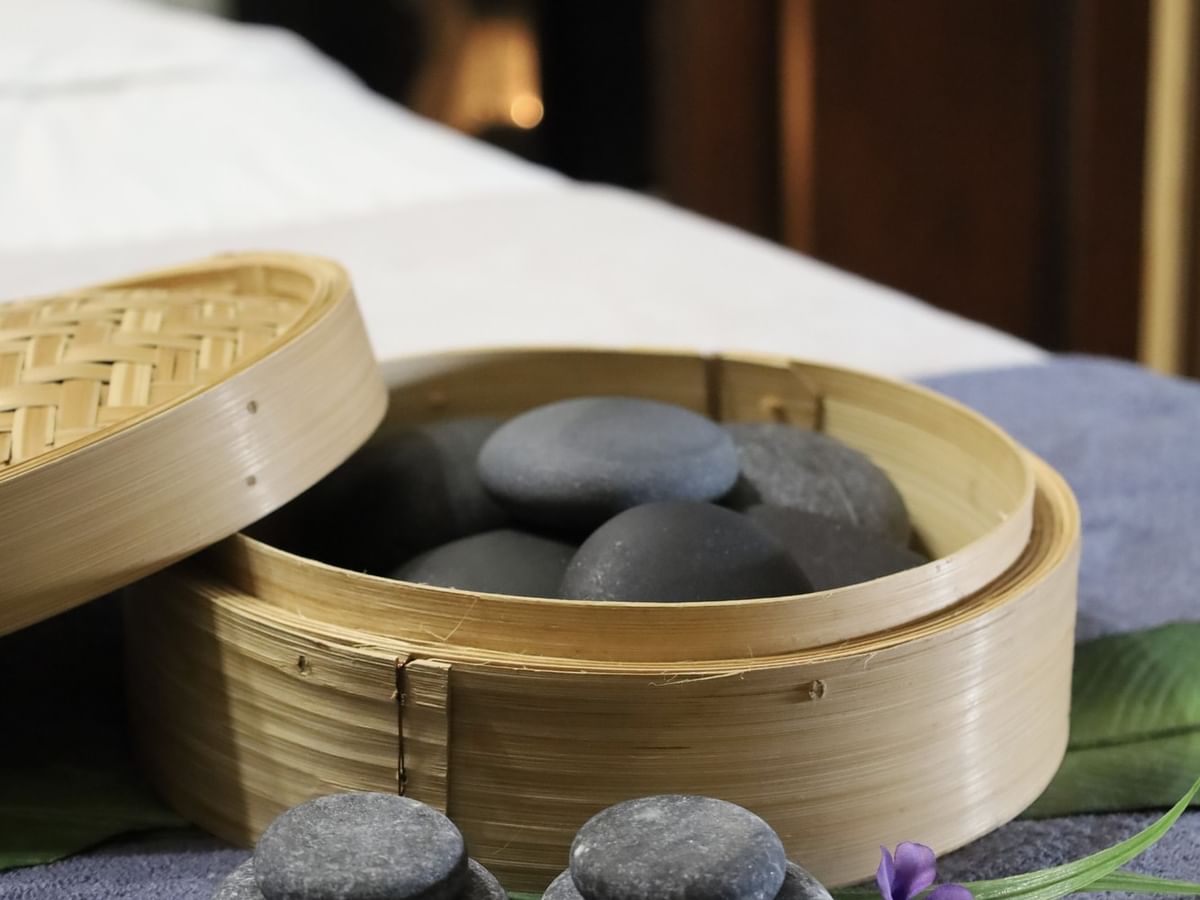 Smooth black stones in a bamboo steamer by a purple flower under soft light at Arlington Resort Hotel & Spa