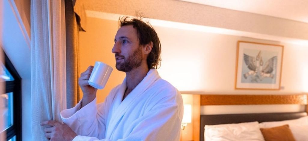 Guest in a bathrobe enjoying morning coffee by the window at Listel Whistler, a Coast Hotel.