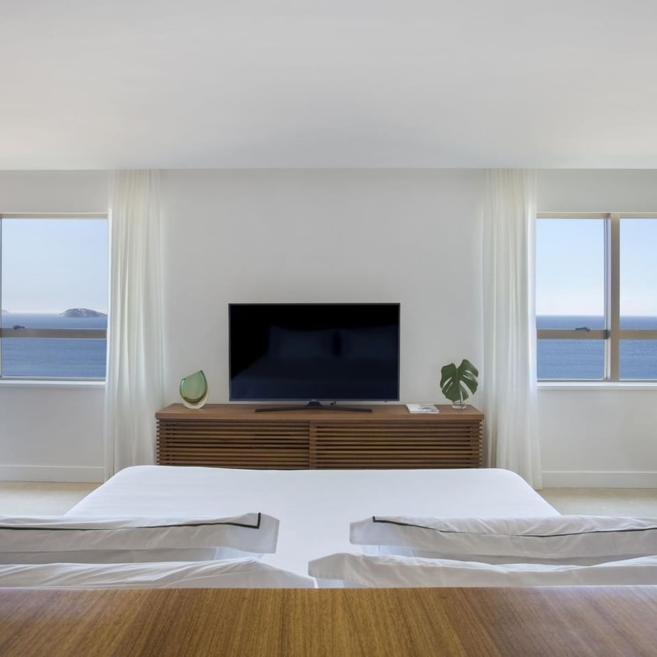 Requintado interior do apartamento com quarto suíte luxo do Janeiro Hotel em um ângulo que mostra a cama king size de frente para a janela com linda vista para o mar