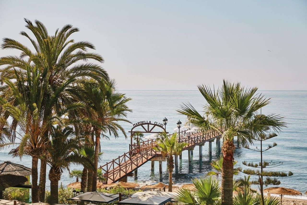 Wooden pier extending into calm blue sea, framed by palm trees at Marbella Club’s scenic beach
