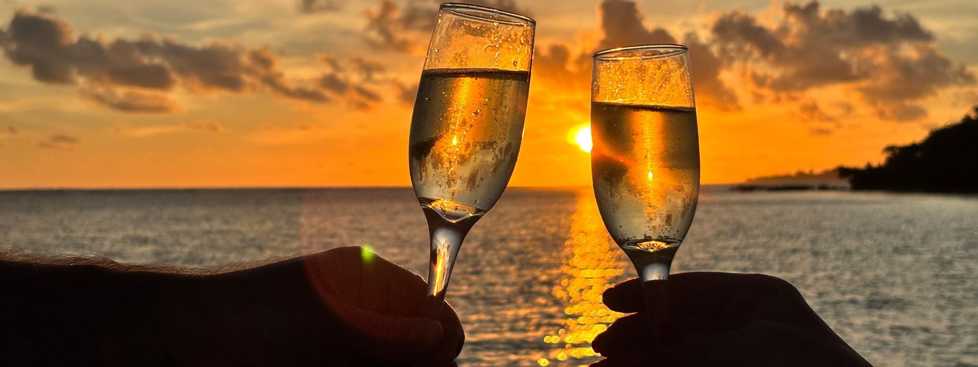 Two hands toasting with champagne glasses at sunset over the sea at Warwick Le Lagon in Efate