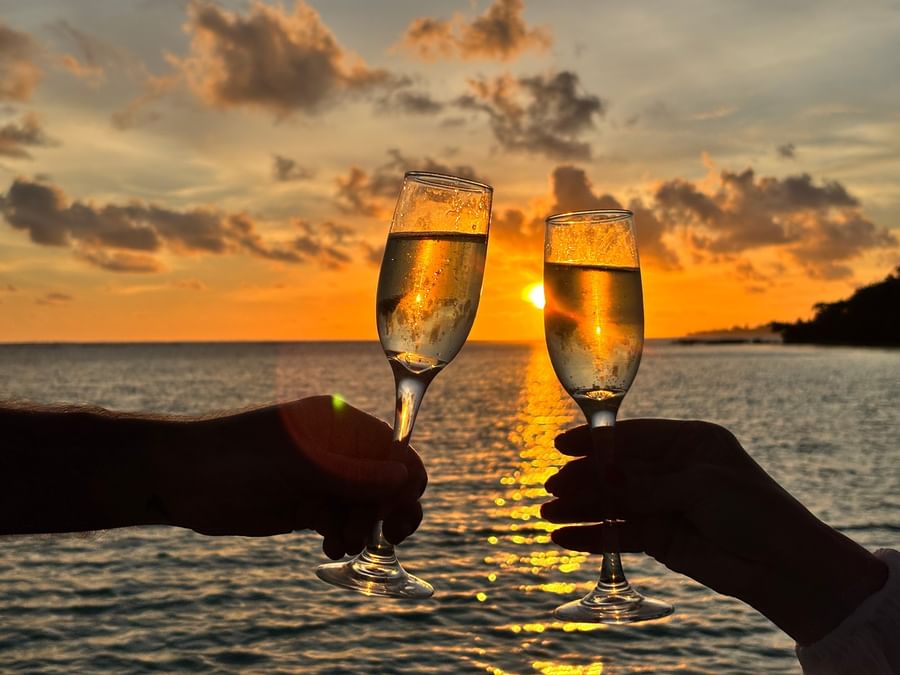 Two hands toasting with champagne glasses at sunset over the sea at Warwick Le Lagon in Efate