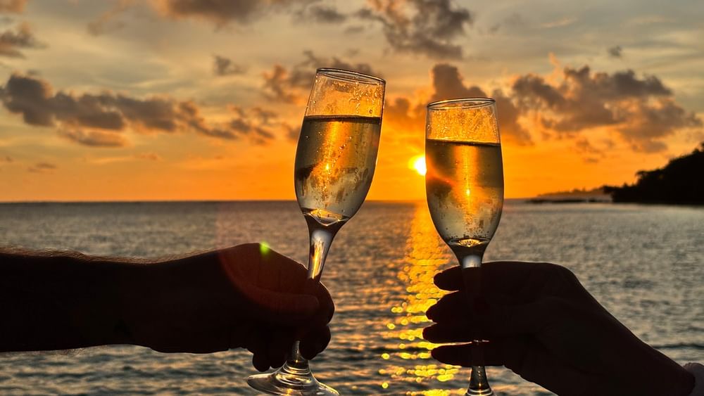 Two hands toasting with champagne glasses at sunset over the sea at Warwick Le Lagon in Efate.