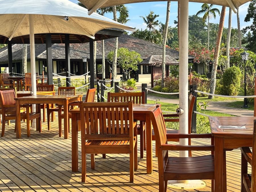 Wooden dining area with tables and chairs under umbrellas at Warwick Le Lagon.