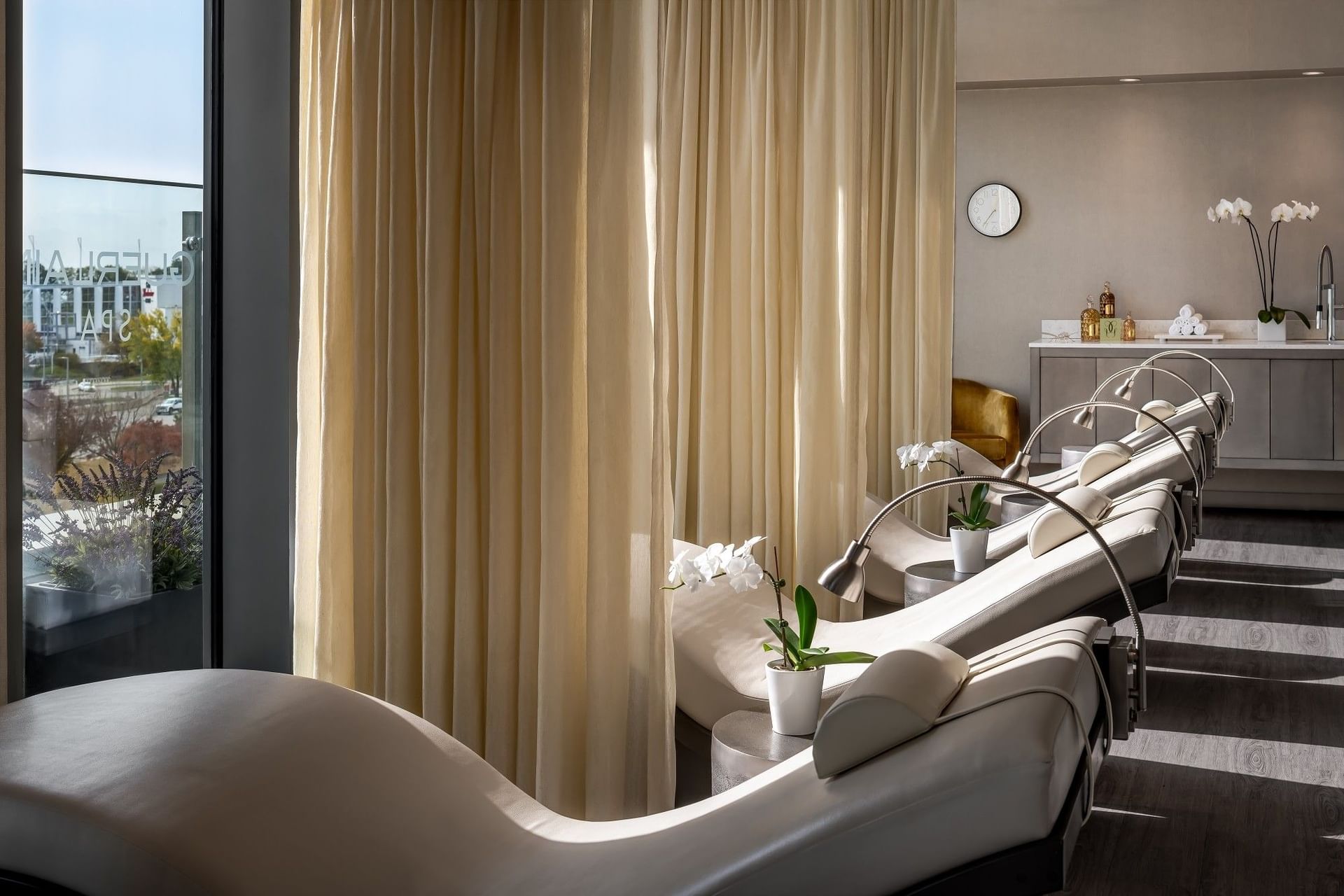 Relaxation loungers inside a Guerlain Spa room with cream curtains and potted white orchids facing glass at Hotel X Toronto