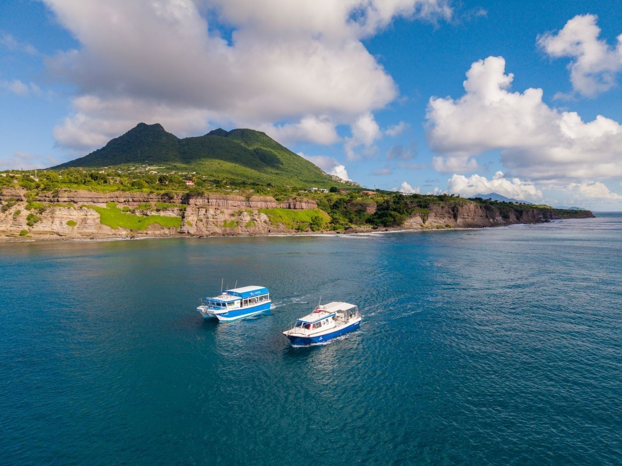 Aerial view of two passenger boats cruising on a clear blue sea along a scenic coastline near Golden Rock Resort