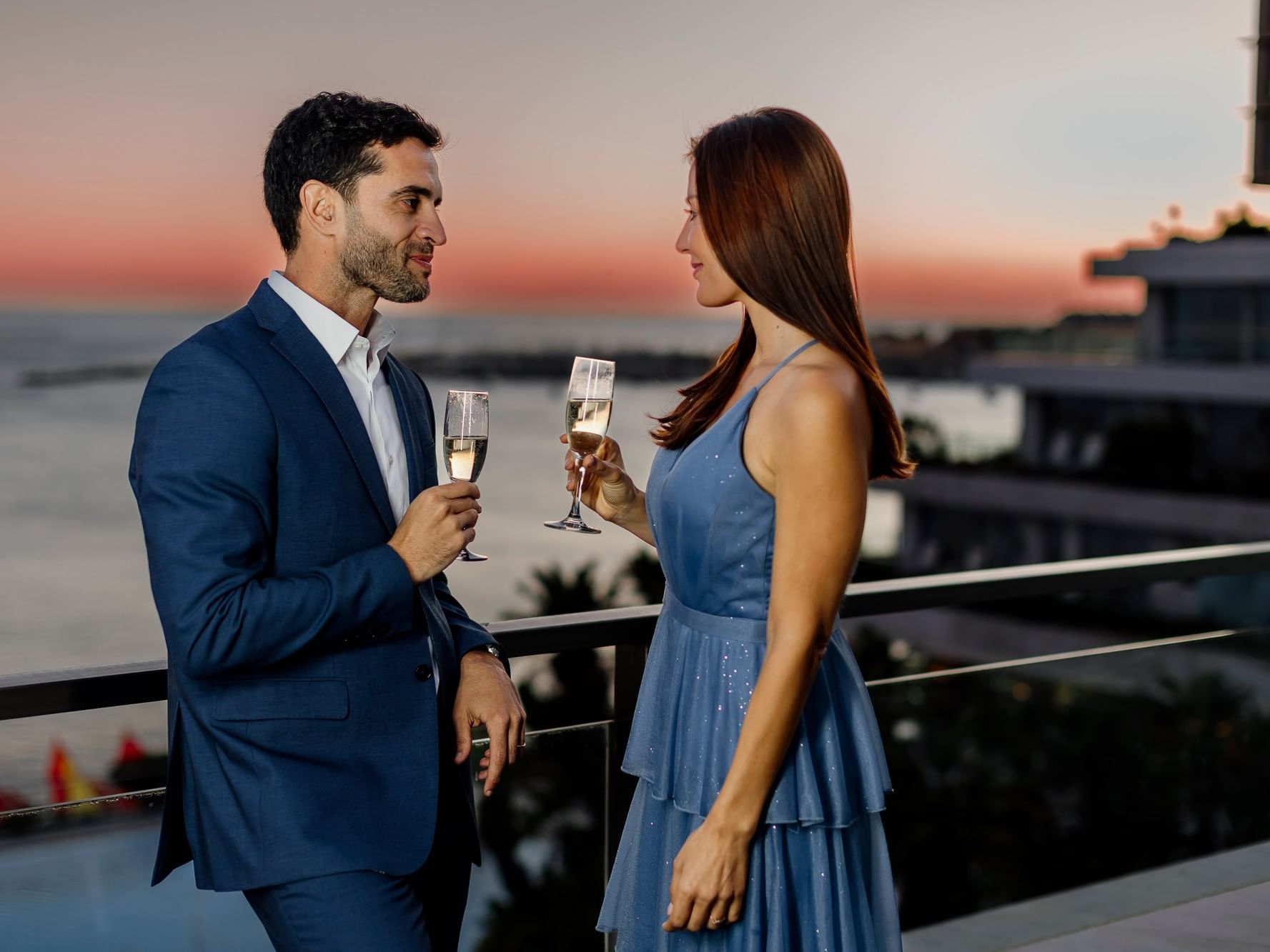 Un couple partage un moment romantique avec du champagne sur un balcon surplombant le coucher du soleil.