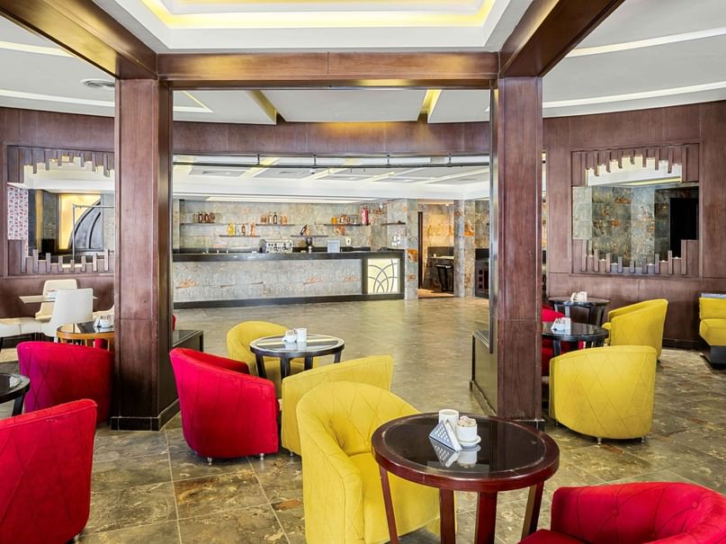 A lounge area with red and yellow chairs, round tables, and a reception desk in the background.