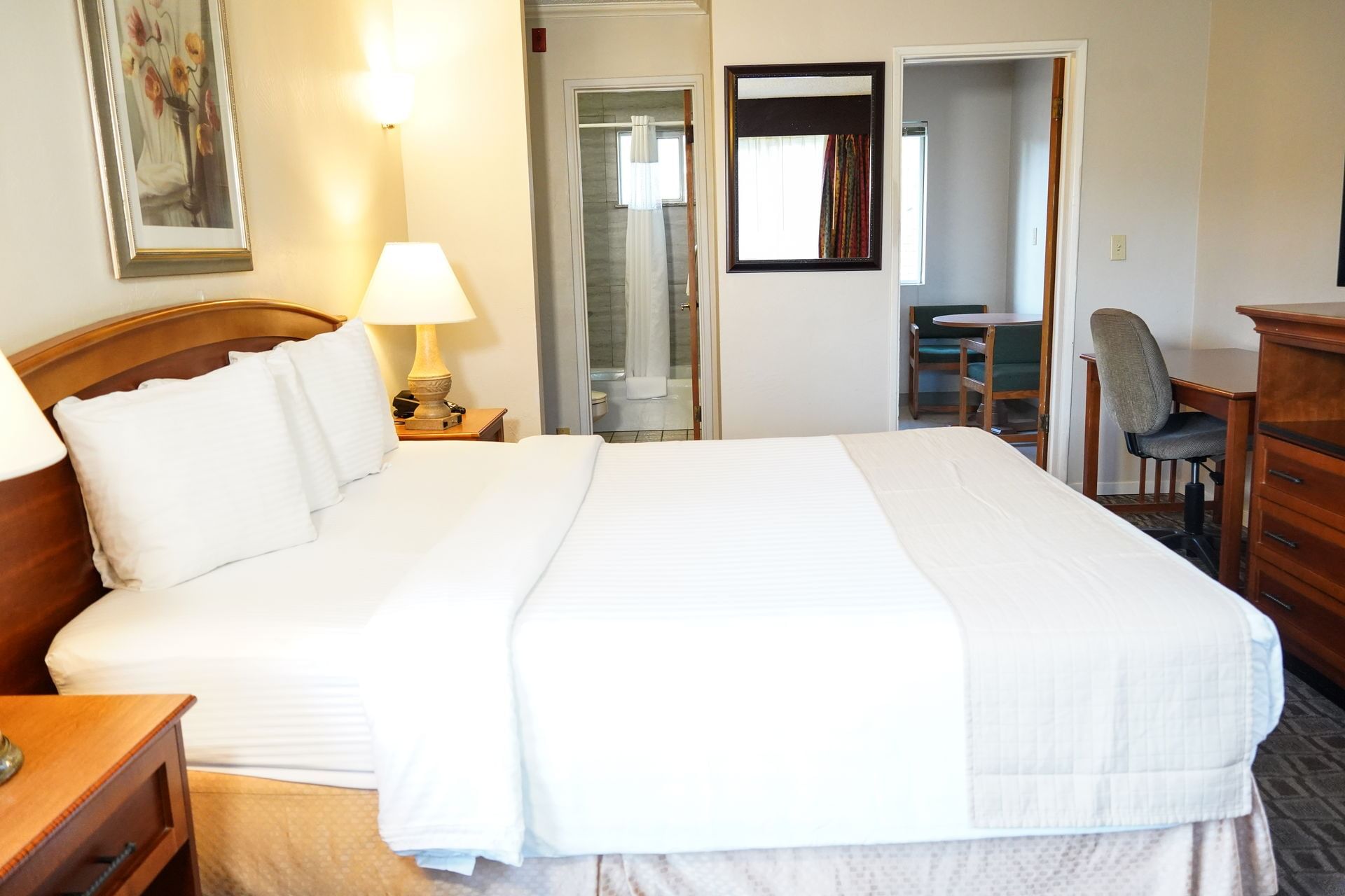 A standard hotel room with a bed, nightstand, lamp, desk, and chair.