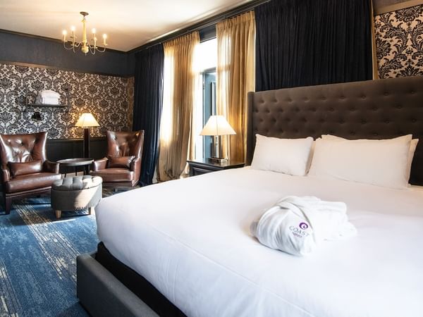 Hotel room with king bed, bath robe, armchair, coffee table, and window