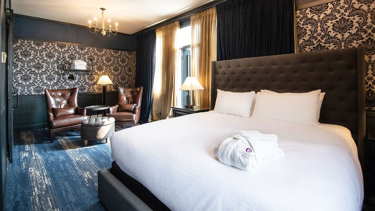 Hotel room with king bed, bath robe, armchair, coffee table, and window