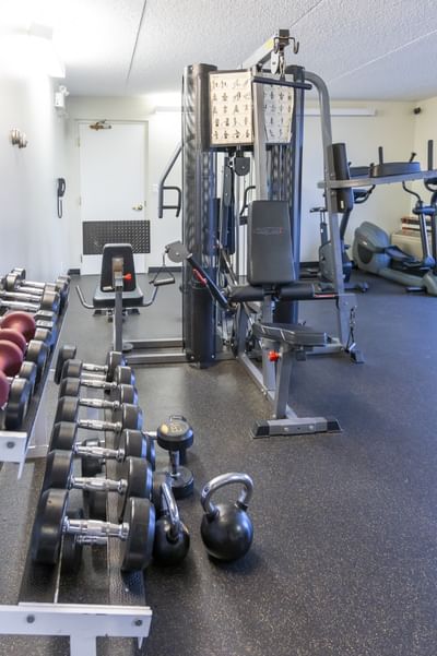 Weight rack with dumbbells by a multi-gym machine under bright white lights in a gym at Rodd Miramichi River
