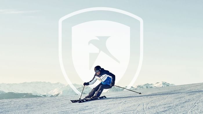 Skifahrer auf schneebedeckter Piste mit Bergpanorama und Logo im Vordergrund.