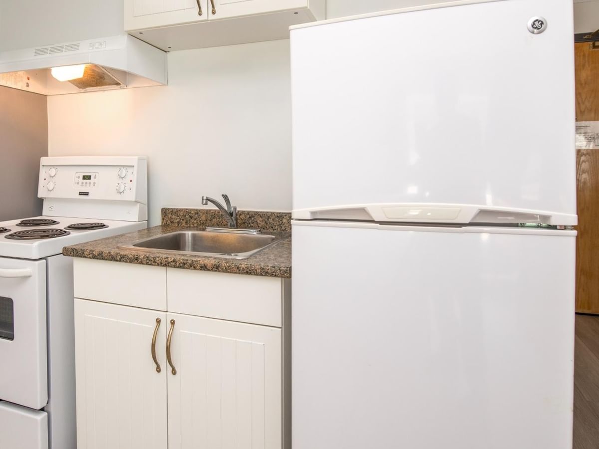 White kitchen with stove, refrigerator, and cabinets, with wooden door on the right.