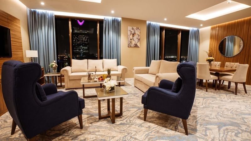 Elegant living area with sofas by a dining set under blue drapes at night in Royal Suite at Cantonal Hotel by Warwick Riyadh