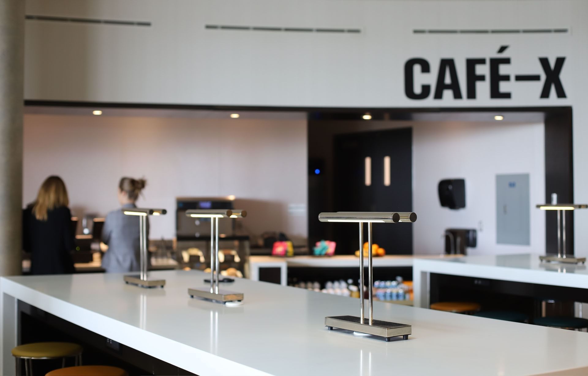 White counter with sleek desk lamps and high stools facing the Cafe-X counter with staff members at Hotel X Toronto