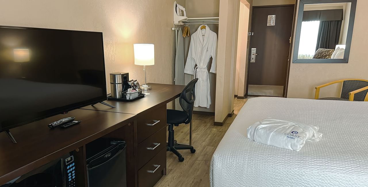 Hotel room with bed, TV, table, mini fridge, and bath robe