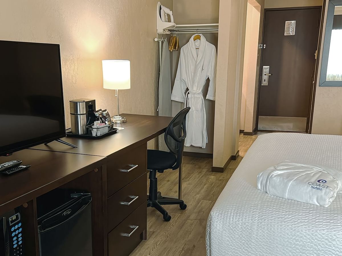 Bed, bath robes, table, chairs, tv, mini fridge in a hotel room