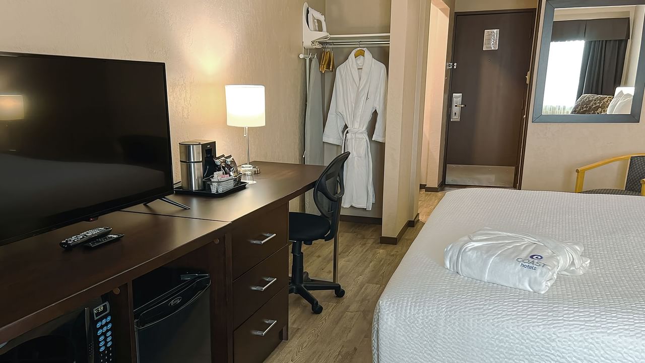 Bed, bath robes, table, chairs, tv, mini fridge in a hotel room