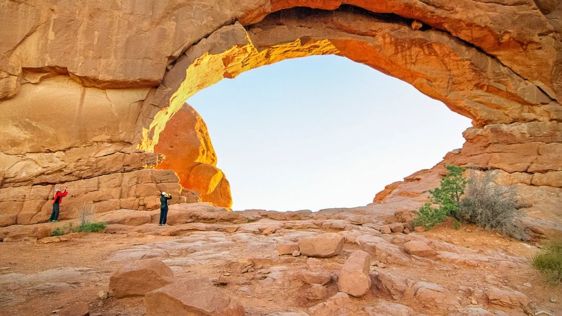 a large rock arch with two people standing in front of it