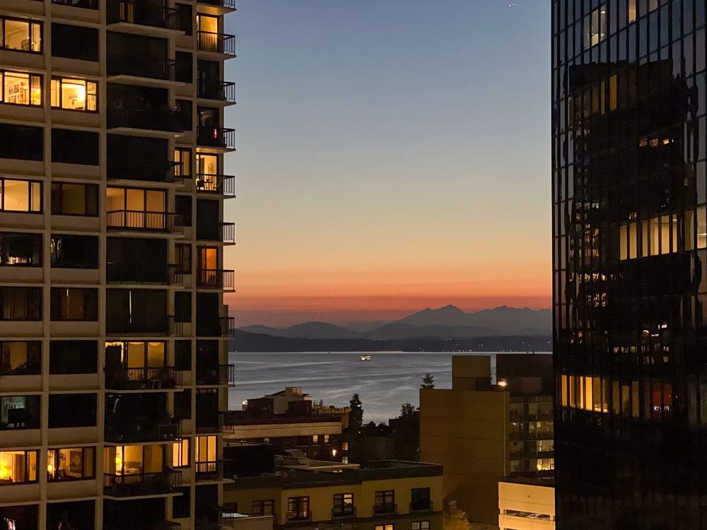 City skyline at dusk with mountain views in the distance by glowing windows near Warwick Seattle