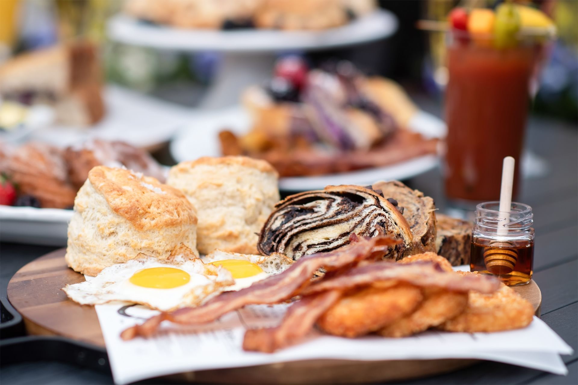 Breakfast platter with eggs, bacon, biscuits, bread and honey arranged on a wooden board with a cold drink at The Brook