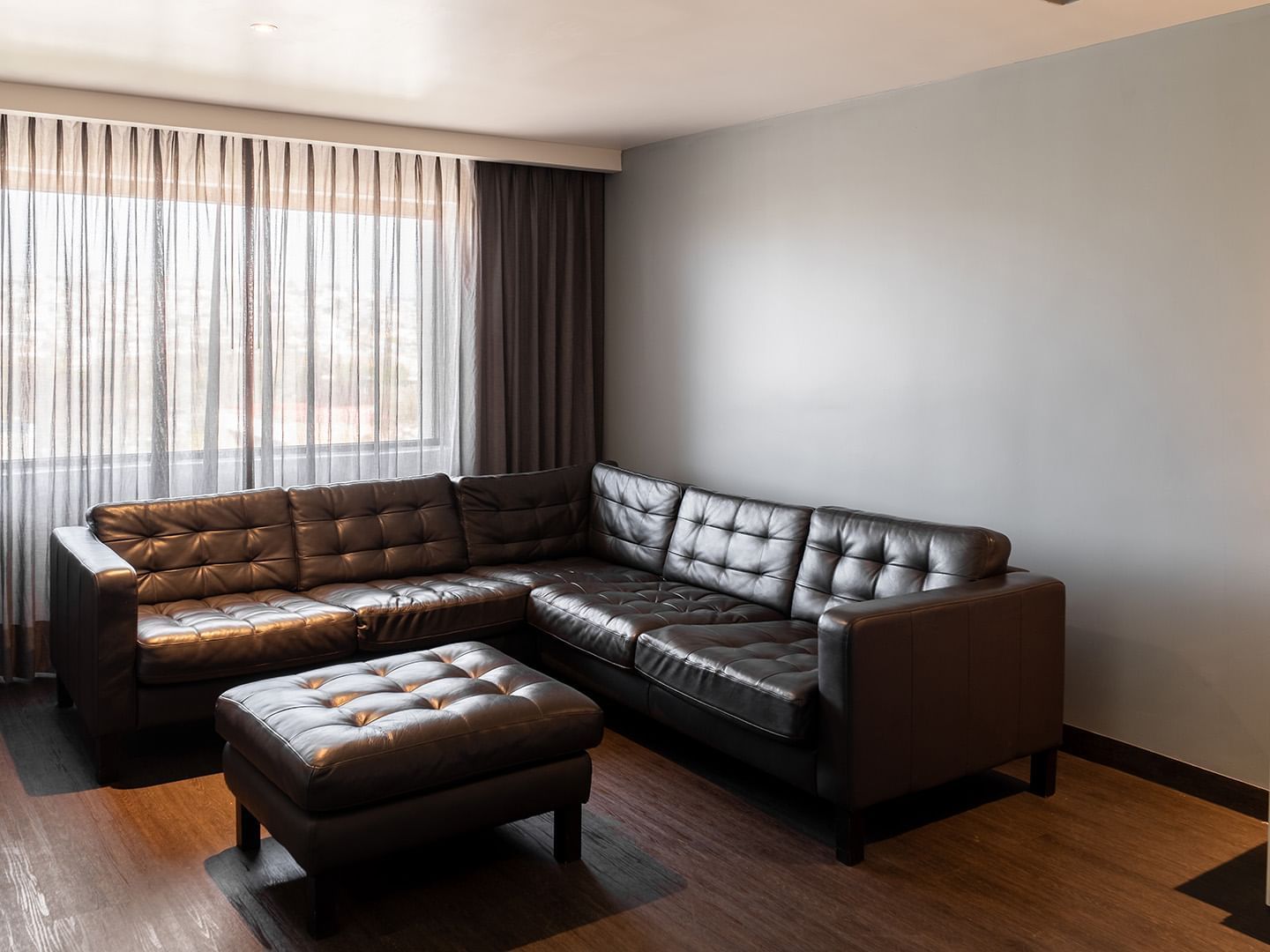 King Junior Suite featuring a dark L-shaped leather sofa, matching ottoman, and curtains at Real Inn Tijuana